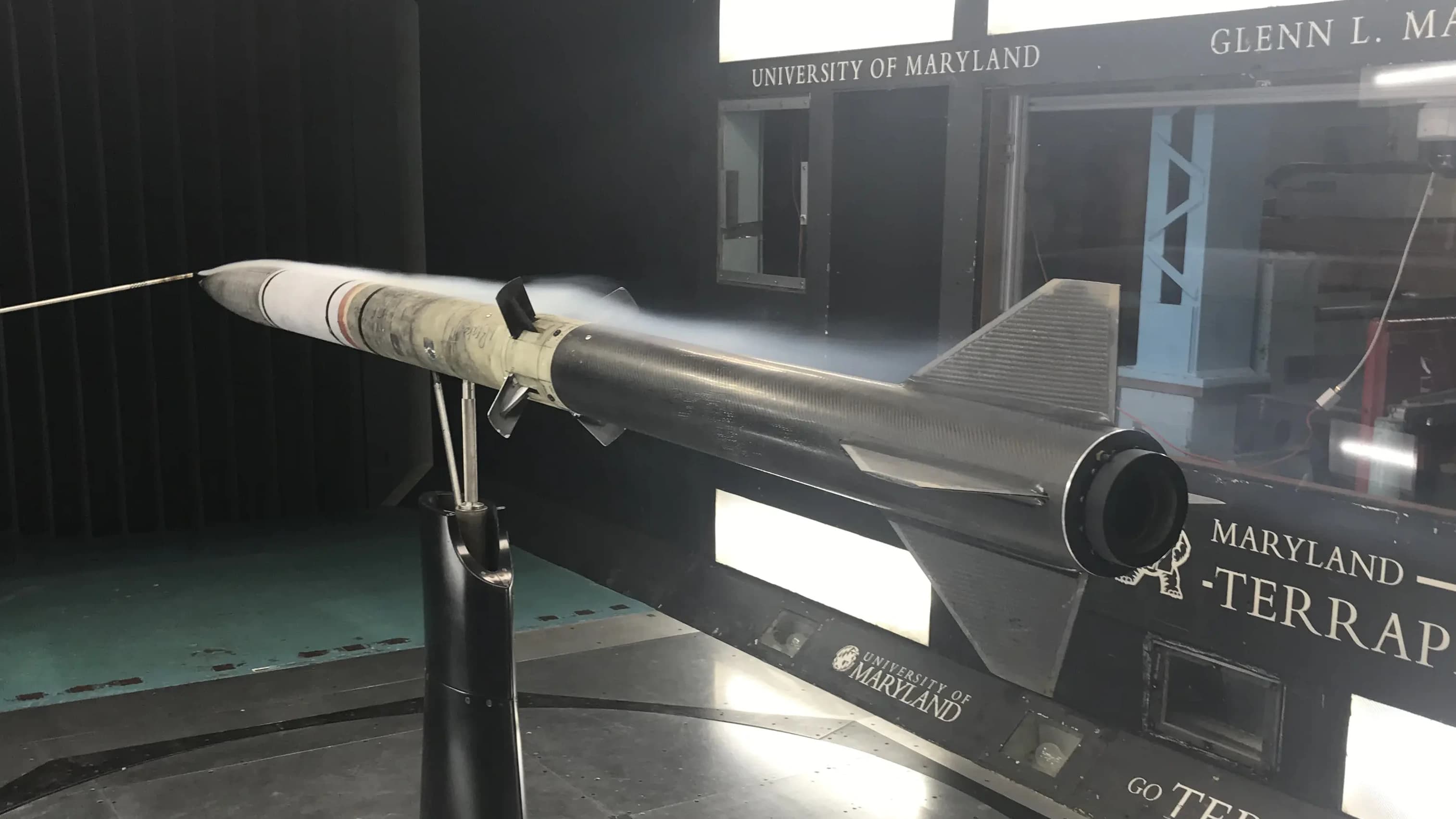 Image of the complete rocket in a windtunnel horizontally, with the airbrakes deployed, and smoke visualization over the airbrake flaps